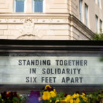 A building sign during the COVID-19 pandemic that reads Standing Together in Solidarity Six Feet Apart