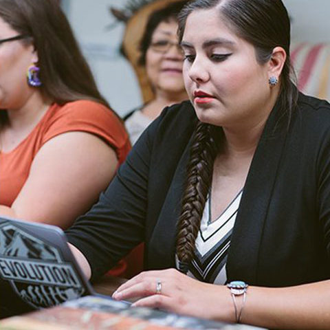 Indigenous woman in a classroom reading on a laptop.