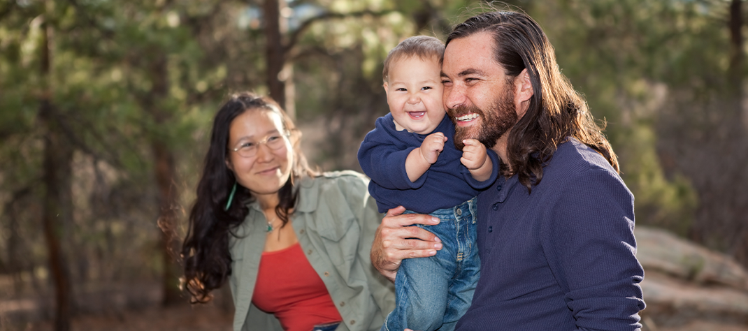 Family of three enjoying a day hiking in nature. Mother, baby, and father are all smiling.