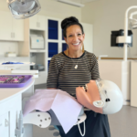 A woman smiling in a white room with dental equipment.